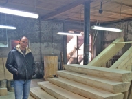 Заказчик Алексей в столярной мастерской на фоне лестницы из кедрового лафета